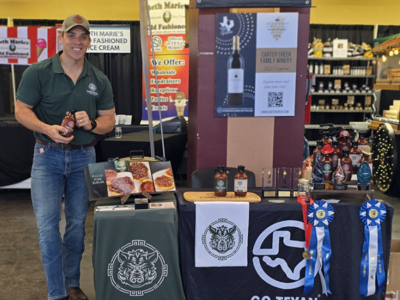 David McCulley holding Torcatha BBQ sauce at a market with other vendors.