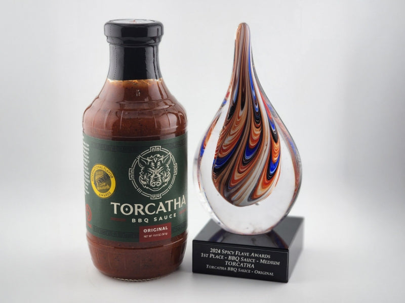 A bottle of Torcatha Original BBQ Sauce next to a decorative glass trophy from the 2024 Spicy Flave Awards.