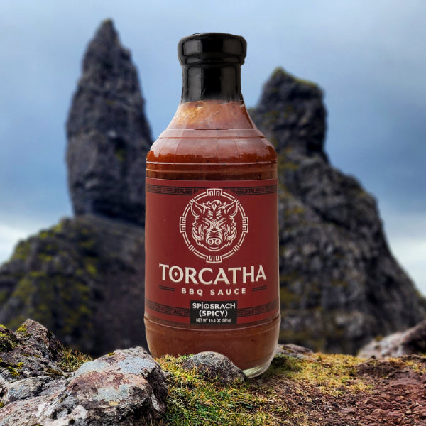 Torcatha Spìosrach BBQ Sauce bottle with a red label, sitting on a mossy rock against a rocky background.