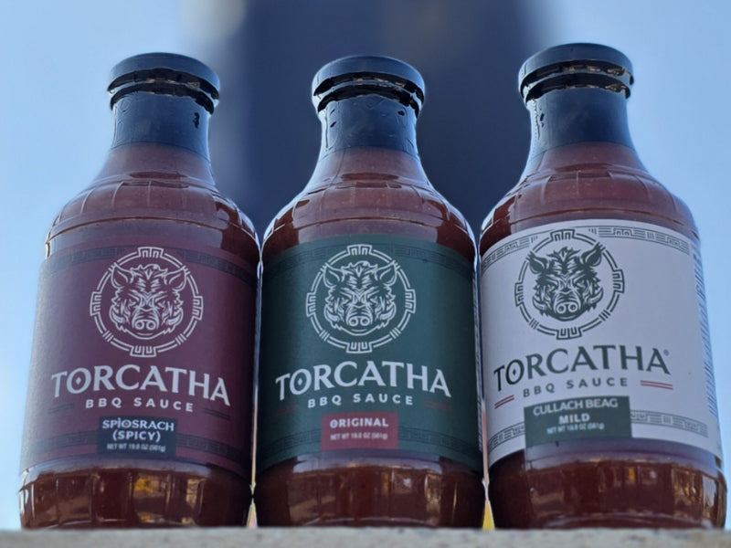 Three bottles of Torcatha BBQ sauce, Spicy, Original, and Mild with a blue background.