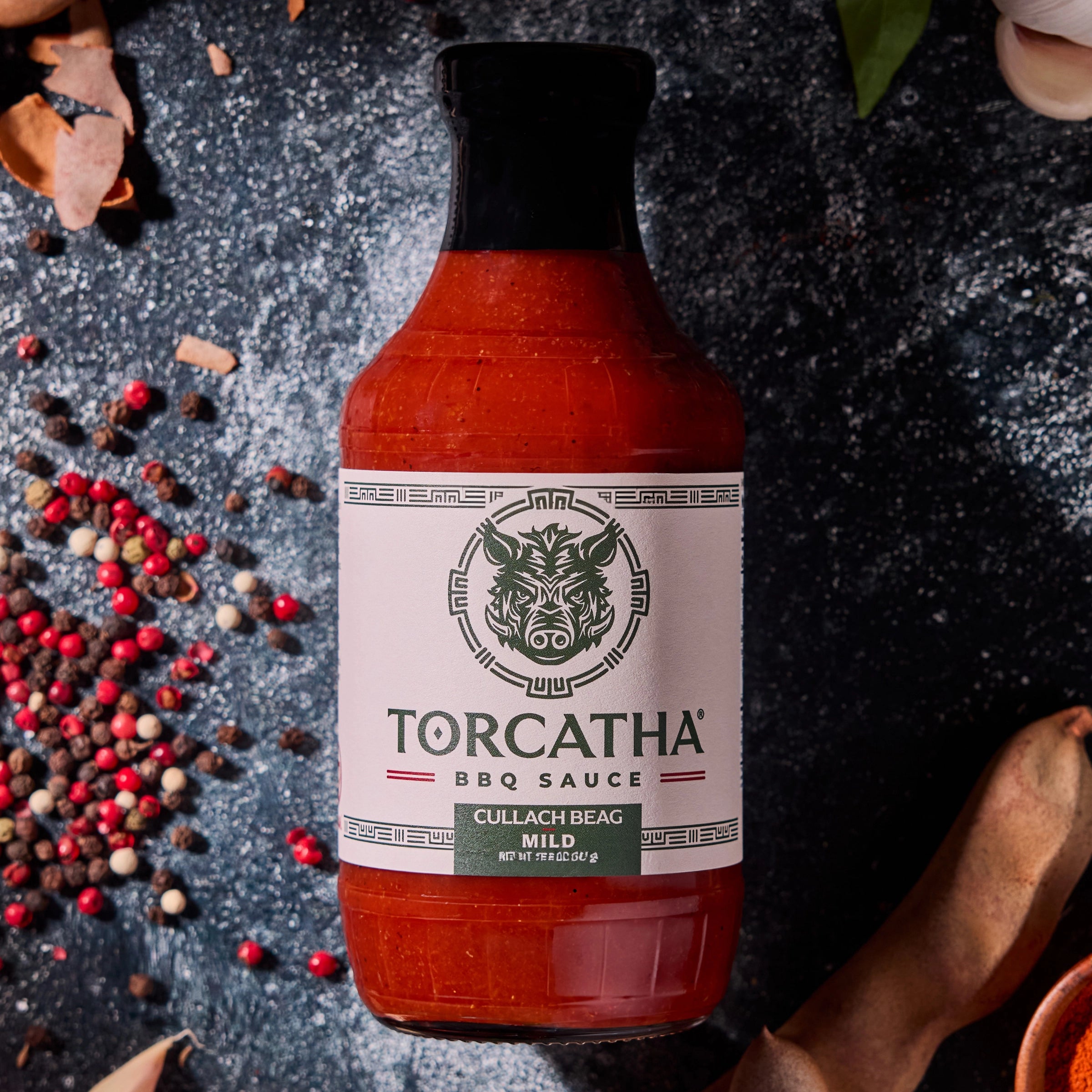 A Torcatha BBQ Sauce bottle, Cullach Beag (Mild flavor), surrounded by ingredients on a dark surface.