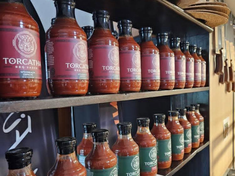 Various bottles of Torcatha BBQ sauces with red and green labels on a shelf.