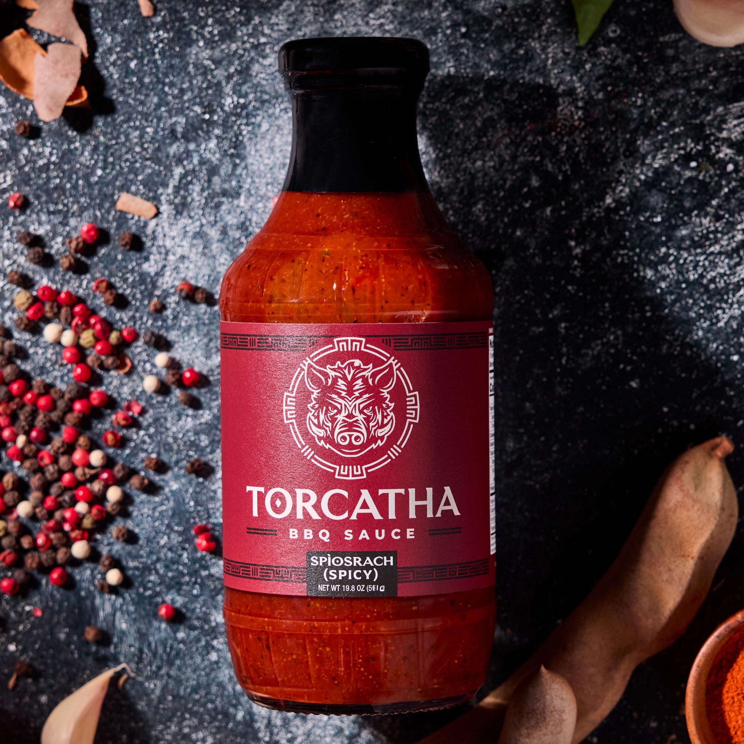 A Spìosrach (Spicy) Torcatha BBQ Sauce bottle, surrounded by ingredients on a dark surface.