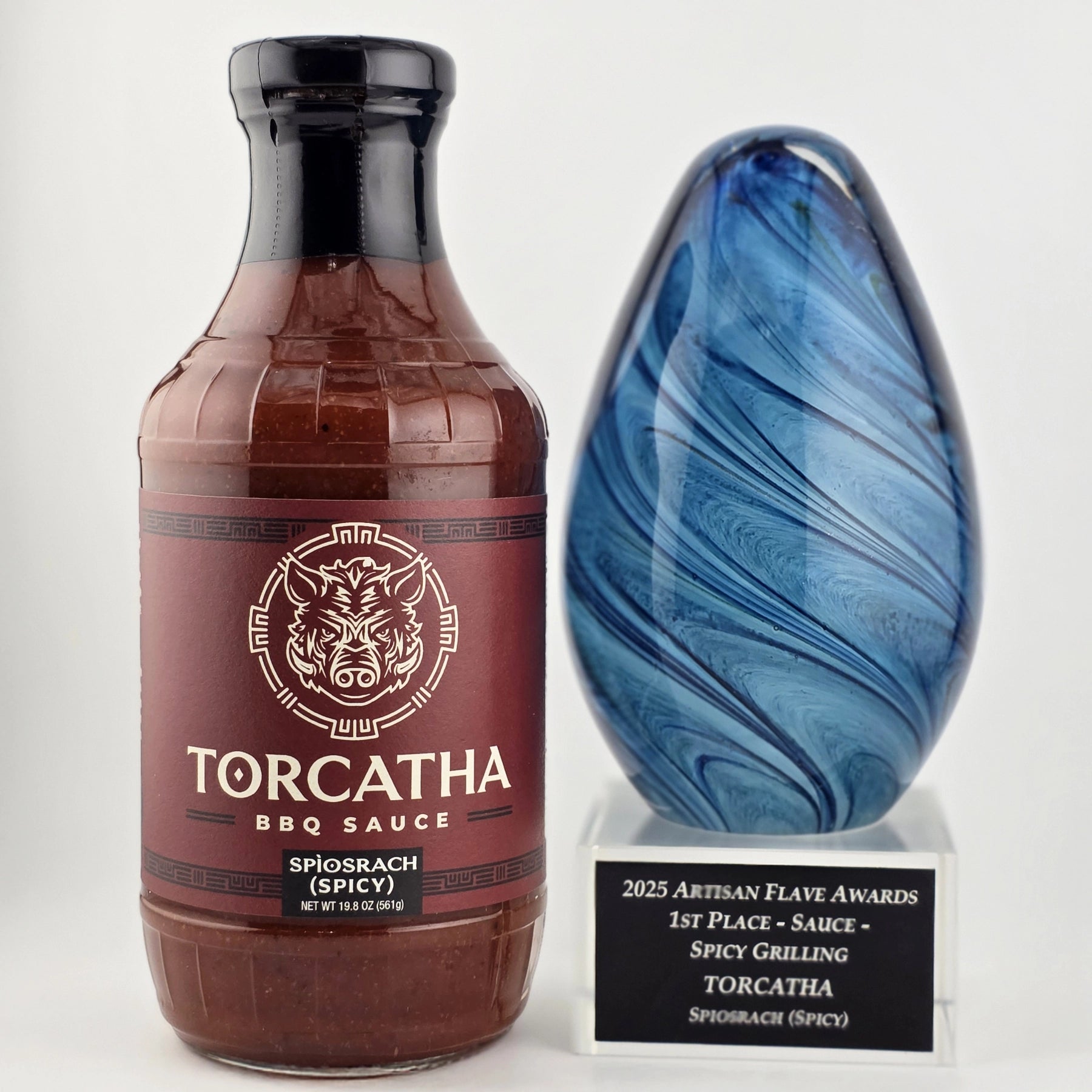 A bottle of Torcatha Spìosrach Spicy BBQ Sauce next to a blue trophy for the 2025 Artisan Flave Award, 1st Place Spicy Grilling Sauce.