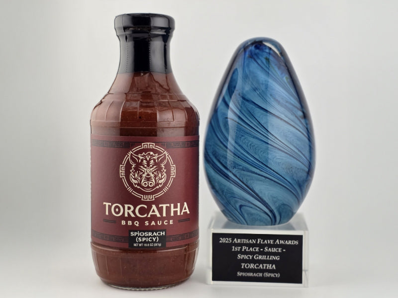 A bottle of Torcatha Spìosrach Spicy BBQ Sauce next to a blue trophy for the 2025 Artisan Flave Award, 1st Place Spicy Grilling Sauce. 
