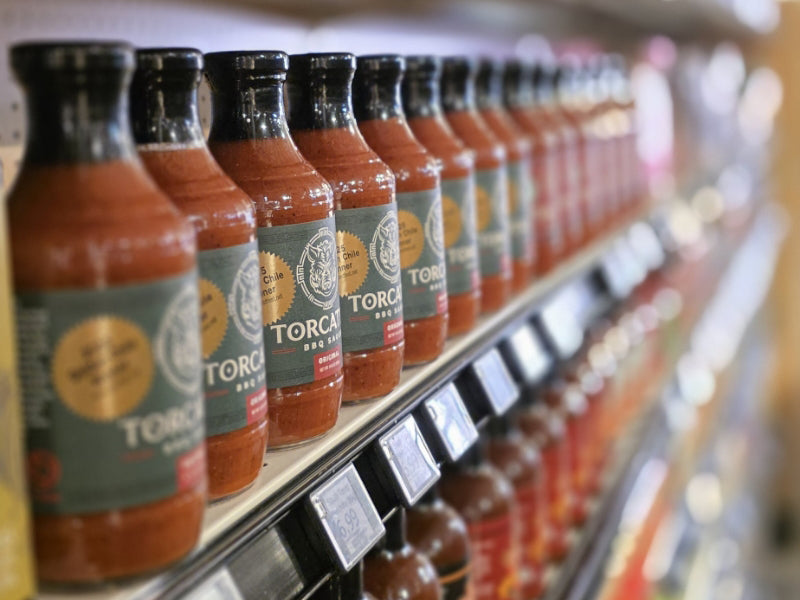 A row of Torcatha BBQ Sauce bottles with green labels displayed on a store shelf.