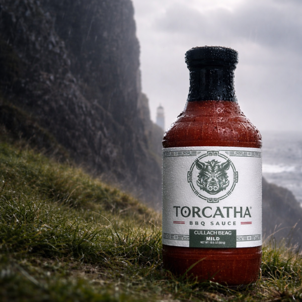 Bottle of Torcatha BBQ sauce on grass with a mountainous background